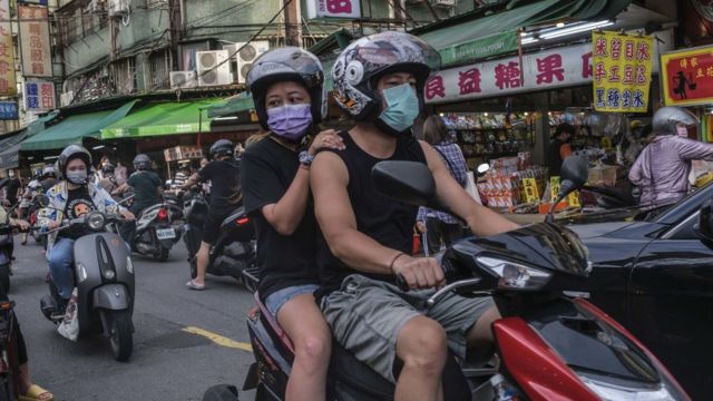 A man and a woman walk through the market on a motorcycle on the streets of Taipei (6/7/2022)
