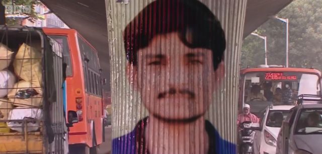 Imagem mostra o trânsito de carros em rua da Índia e, no centro, um pilar com a pintura do rosto de Kaalu, homem de 26 anos que foi morto pela população após ser apontado como sequestrador - por causa de um vídeo falso que circulou no WhatsApp e deixou as pessoas em pânico.