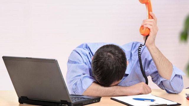 Un empleado con expresión de desesperación, frente a una laptop y con un teléfono