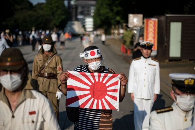 Mężczyzna trzyma flagę Rising Sun, między innymi ubrany w mundur Armii Cesarskiej i Marynarki Wojennej podczas wydarzenia 15 sierpnia 2020 r. w Tokio z okazji 75. rocznicy kapitulacji Japonii podczas II wojny światowej.