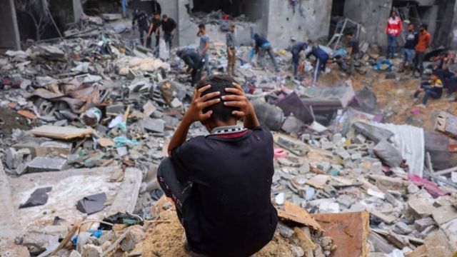 イスラエル国防軍の空爆でがれきと化した建物の中から所持品を集める人々と頭を抱えてしゃがみ込む子供（2023年11月、ガザ地区南部ラファ）