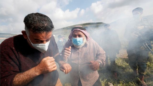 Palestinian demonstrators react to tear gas fired by Israeli troops during a protest against Israeli settlements