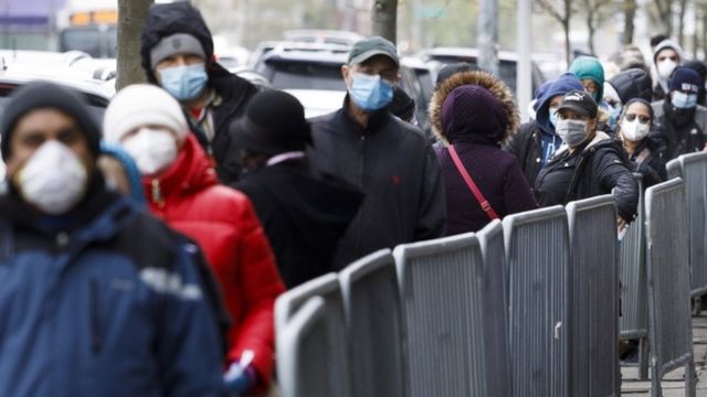Dezenas de pessoas enfileiradas em área externa, com máscaras e roupas de frio