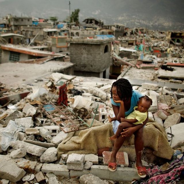 Mujer con bebé sentada sobre las ruinas de lo que era su casa antes del terremoto de 2010 en Haití.