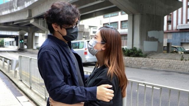 Pro-democracy activist Sam Cheung hugs his wife as he arrives to report to the police station