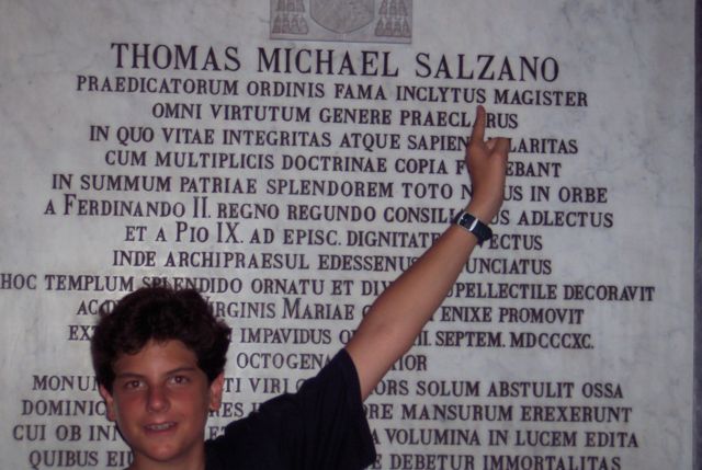 Carlo Acutis em frente a uma placa sobre Thomas Michael Salzano, antigo bispo de Napoli