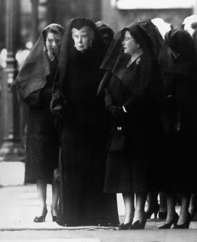 La reina María (centro) observa cómo el cuerpo de su hijo, Jorge VI, es llevado a Westminster Hall, Londres, para el funeral. A su lado, la reina Madre, a la derecha, con los ojos cerrados por el dolor. La reina Isabel II, con velo, se para detrás de su abuela.