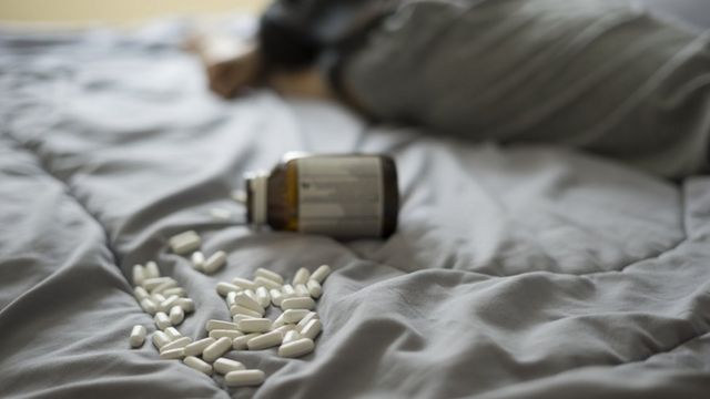 Representación de un suicidio con tabletas de medicina sorbe una cama.