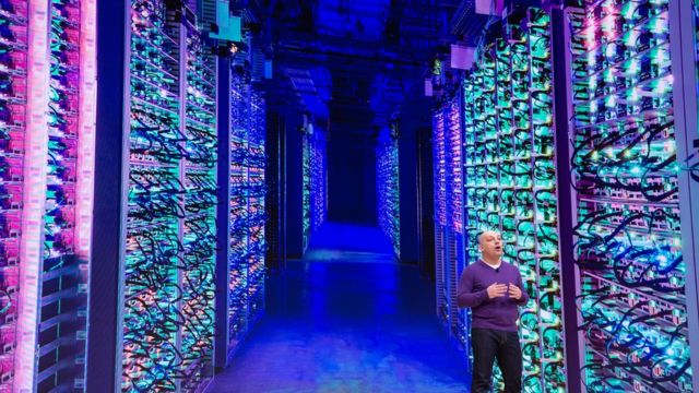 A man standing in a data center with rows and rows of stacked server machines stretching into the distance