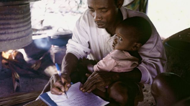 Un homme ecrit sur une feuille avec son enfant dans les bras