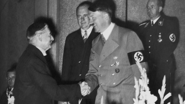 Черно-белое фото, на котором видно, как пожимают руки Адольф Гитлер и невиль Чемберлен