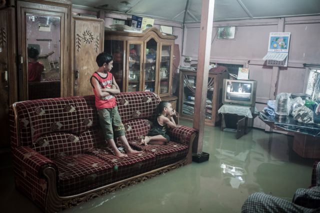 Niños miran la TV en una sala inundada