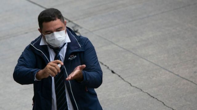 Un hombre con tapabocas rociándose gel antibacterial