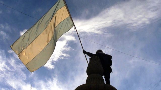 Bandeira argentina na contraluz, segurada por estátua