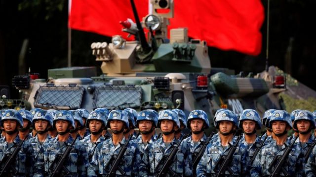 People's Liberation Army (PLA) troops await Xi Jinping at 20th anniversary of city's hand over in Hong Kong. Stand in front of a tank with flag behind
