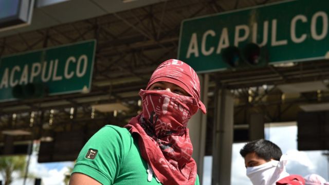 Hombre encapuchado delante de un cartel de Acapulco.