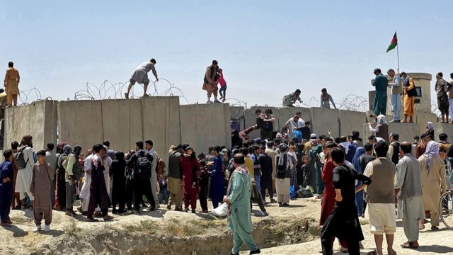 People struggle to cross the boundary wall of Hamid Karzai International Airport to flee Afghanistan