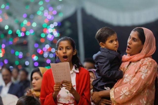 A girl sings along with her mother, who holds a boys in her arms, during a Christmas Eve service at St Andrew's church in Karachi, Pakistan. Photo: 24 December 2021