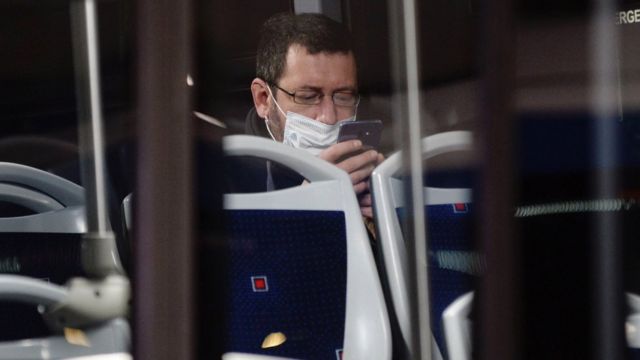 A worker wearing a protective mask looks at his phone on a bus in Valladolid, northern Spain (13 April 2020)