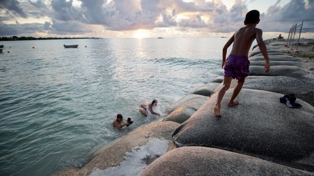 Uma criança caminha sobre sacos de areia empilhados para retardar o avanço do mar
