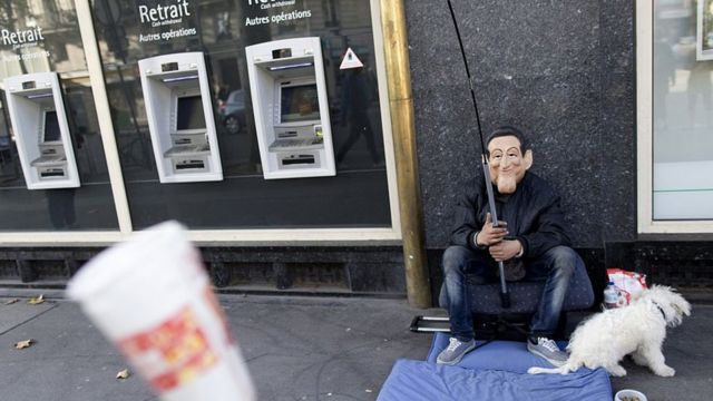 Um homem pedindo dinheiro em frente a caixas eletrônicos