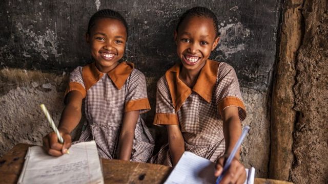 Two girls in uniform smiling with exercise books