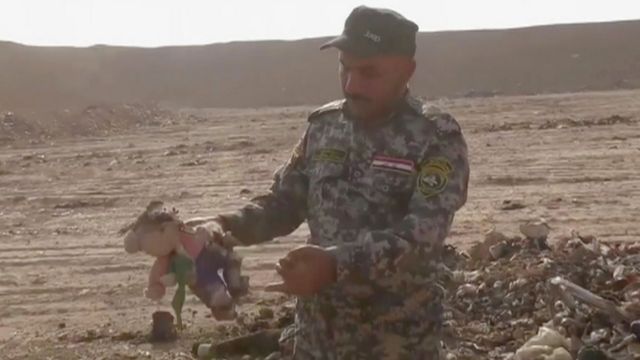 عسكري عراقي يحمل لعبة طفل في المقبرة الجماعية في حمام العليل