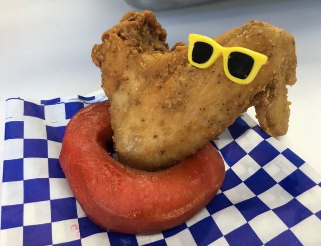 A fried chicken wing placed on a red doughnut wearing sunglasses