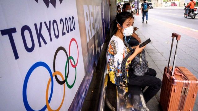 Mulher de máscara no Japão ao lado de logo das Olimpíadas