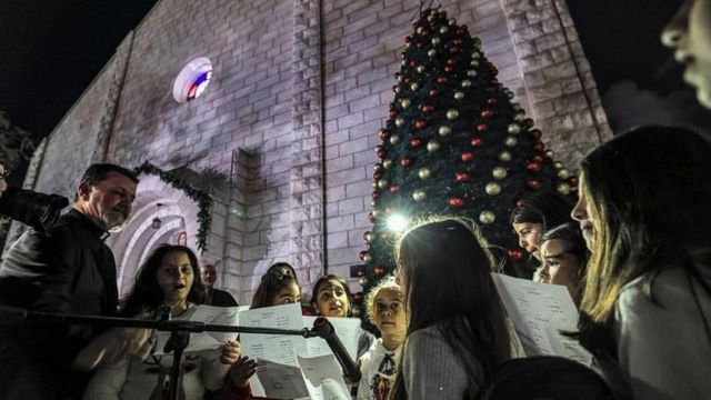 کودکان فلسطینی در کریسمس سال 2021 در مقابل کلیسای خانواده مقدس در غزه آواز می خوانند