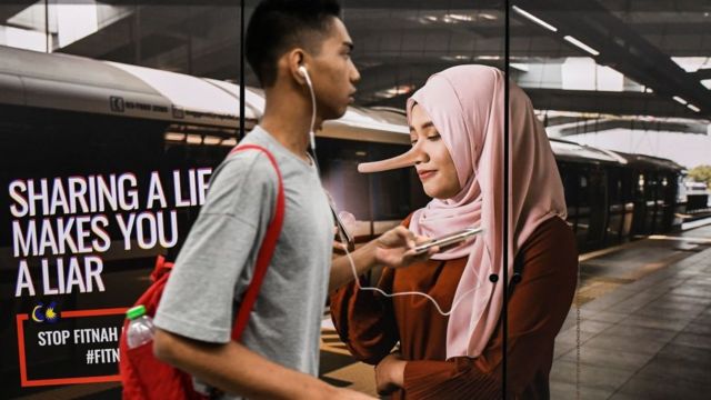 A commuter walks past an advertisement reading 'sharing a lie makes u a liar' at a train station in downtown Kuala Lumpur on March 26, 2018.