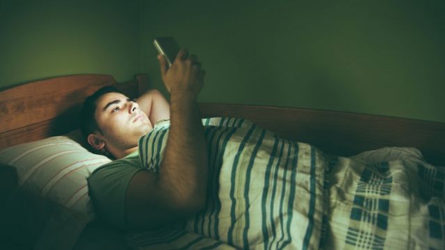A young man looking at his mobile phone in bed.
