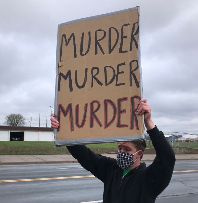 Manifestante a las afueras del Departamento de Policía de Brooklyn Center con un cartel que pone "Asesinato, Asesinato, Asesinato"