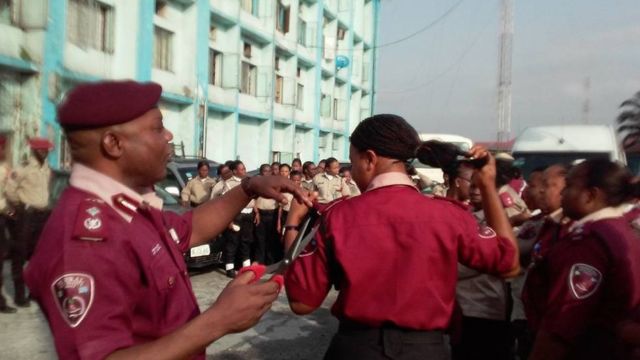 Man in maroon beret cuts a woman's hair in public
