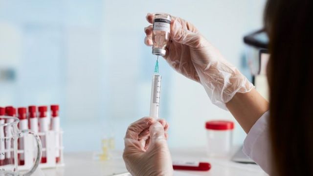 Cientista segura uma seringa e extrai o líquido de uma ampola de vacina