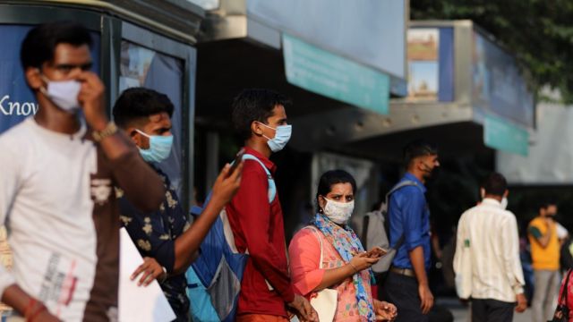 Pessoas na Índia com máscaras esperando por um ônibus