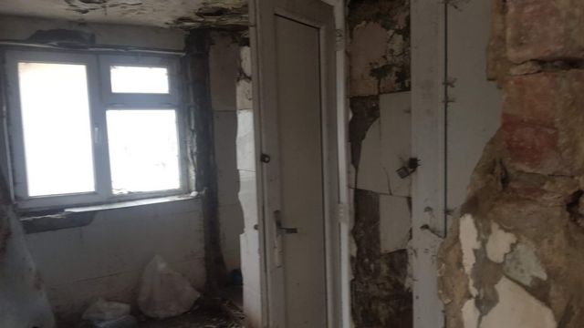 Общий туалет с разбитым кафелем, осыпавшимся потолком и стенами.