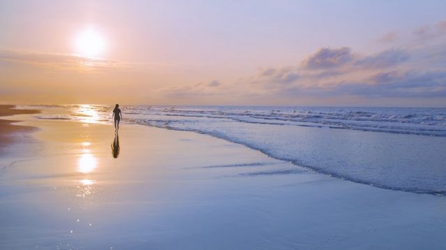 Persona caminando en playa al amanecer