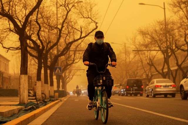 早高峰期間，一名北京居民冒著沙塵在路上騎車。