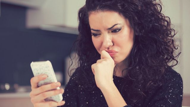 Mujer joven mirando confusa a su celular