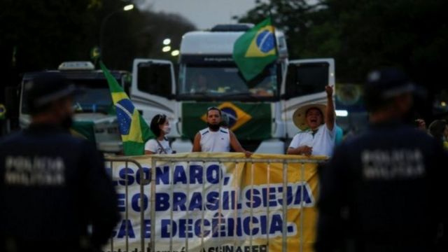 Caminhoneiros protestam com bandeira do Brasil e cartaz favorável a Bolsonaro