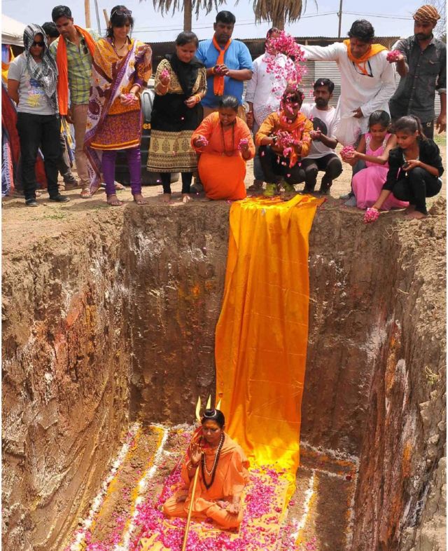 Devotees of Indian Hindu Akhara leader Trikal Bhawanta shower her with rose petals as she is sat inside a deep hole in the ground, preparing to undergo a burial ritual on 26 April 2016