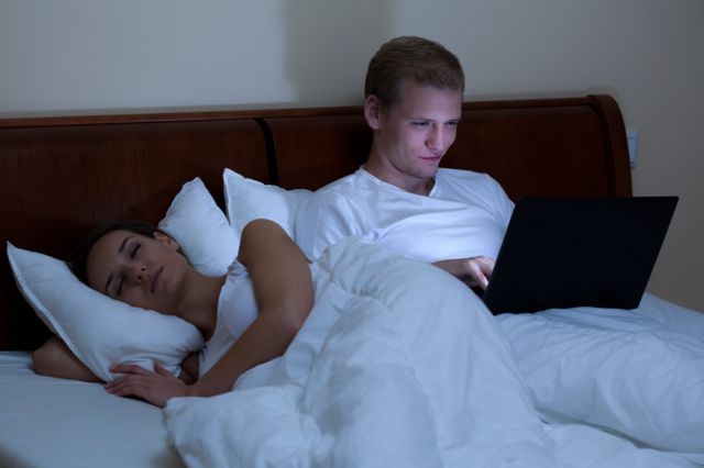 Hombre chateando en las redes sociales con amigos mientras su esposa duerme