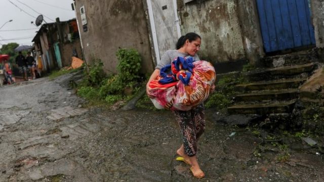 A woman carries cloths as she leaves a mudslide site in Guarujá, São Paulo state, Brazil. Photo: 3 March 2020
