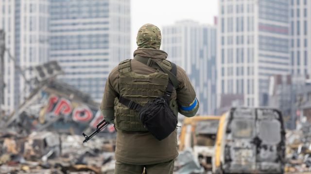 Soldado com metralhadora perto do centro comercial destruído de Retroville após bombardeio russo