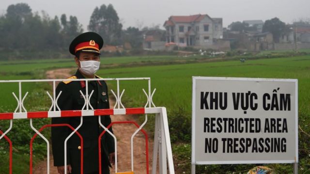 A Vietnamese People's Army officer wearing a protective facemask amid concerns of the COVID-19 coronavirus stands next to a sign warning about the restricted area set up in the Son Loi commune in Vinh Phuc province on February 20, 2020.