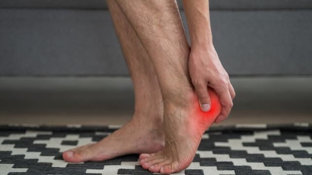 Man holds heel which is red, signaling plantar fasciitis