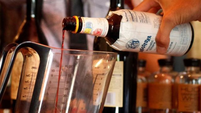 Un bartender echa unas gotas de amargo de Angostura en una coctelera.