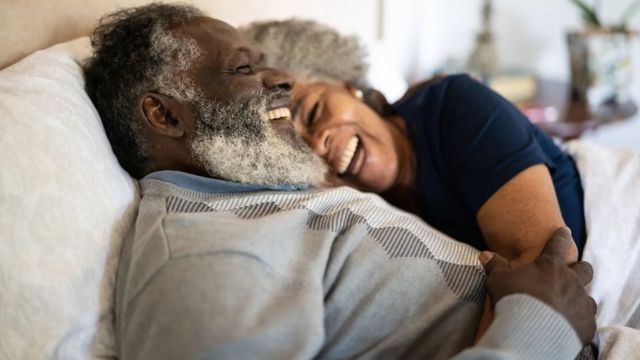 Dos adultos mayores sonriendo en una cama.