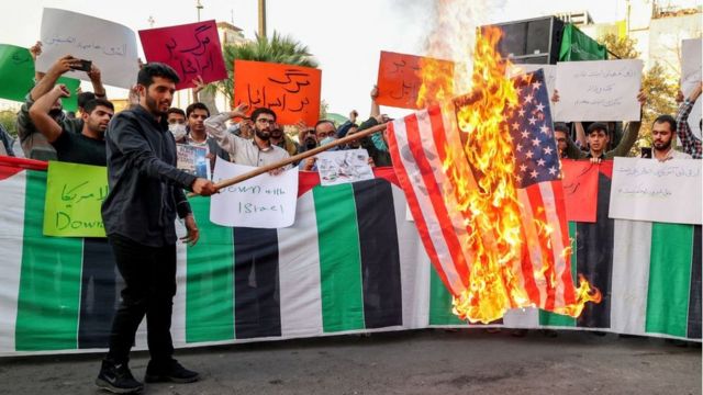 Иранский студент из исламского добровольческого ополчения Басидж сжигает флаг США в столице Тегеране, 16 июля 2022 года.